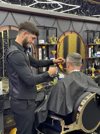 Smiling barber in a black vest trims a customer's hair in a luxury barbershop.
