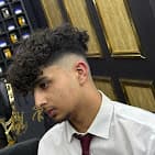 Young man with dark curly hair and skin fade wearing a white shirt and tie.