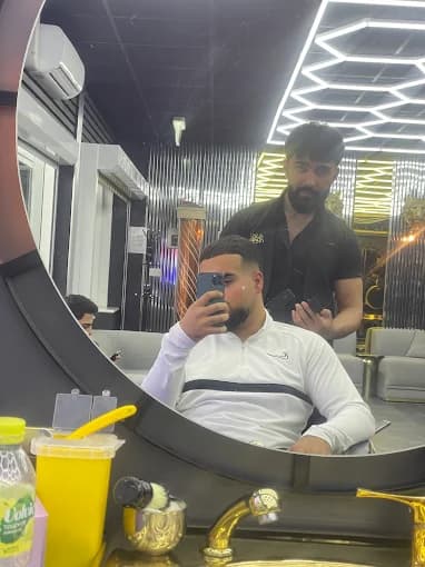 Man takes a mirror selfie while a barber stands behind him in a modern barbershop.